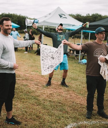 A man celebrating at a race finish line with tents in the background. 