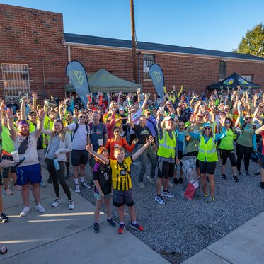 A crowd of runners cheering in a parking lot in front of a pop-up tent and tear drop flags.