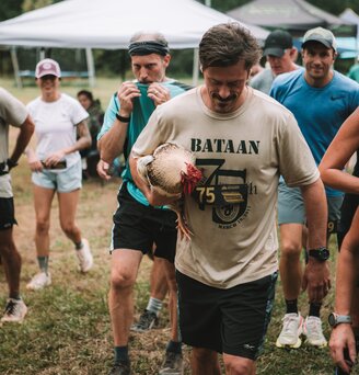 A man carrying a chicken walking with other race participants before a race.